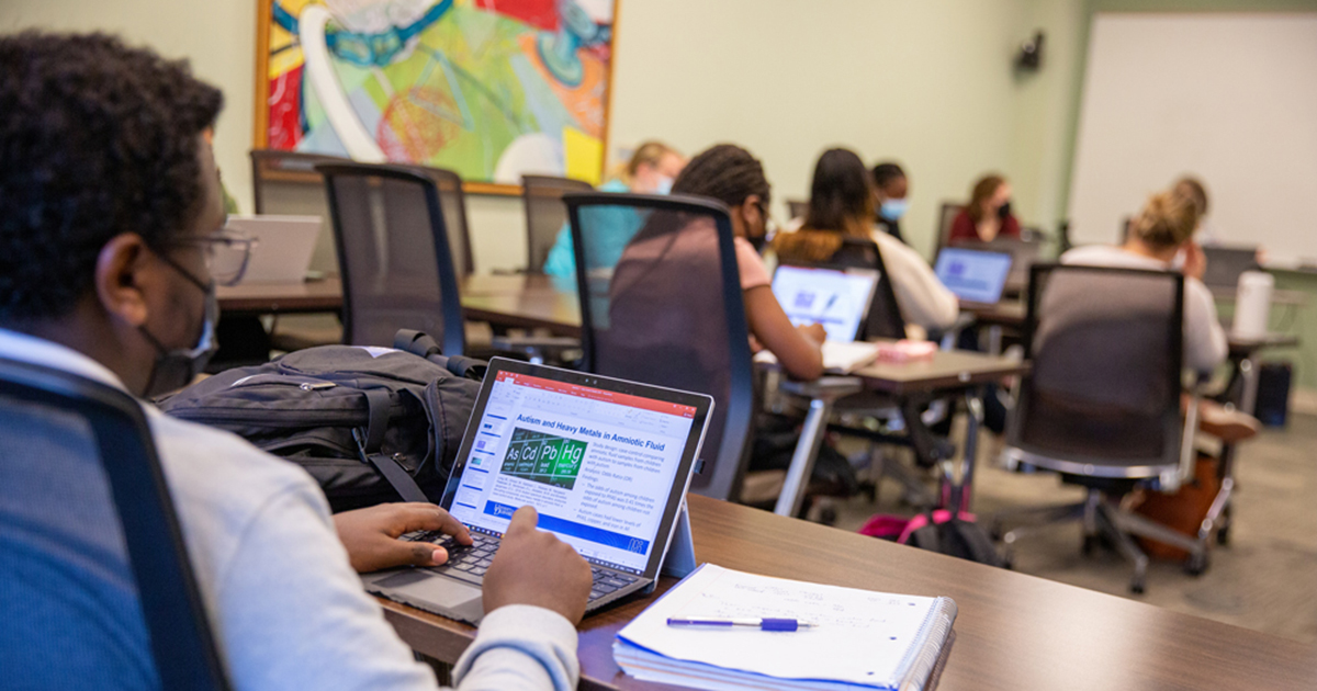 Students work on epidemiology coursework on laptops in a classroom. 