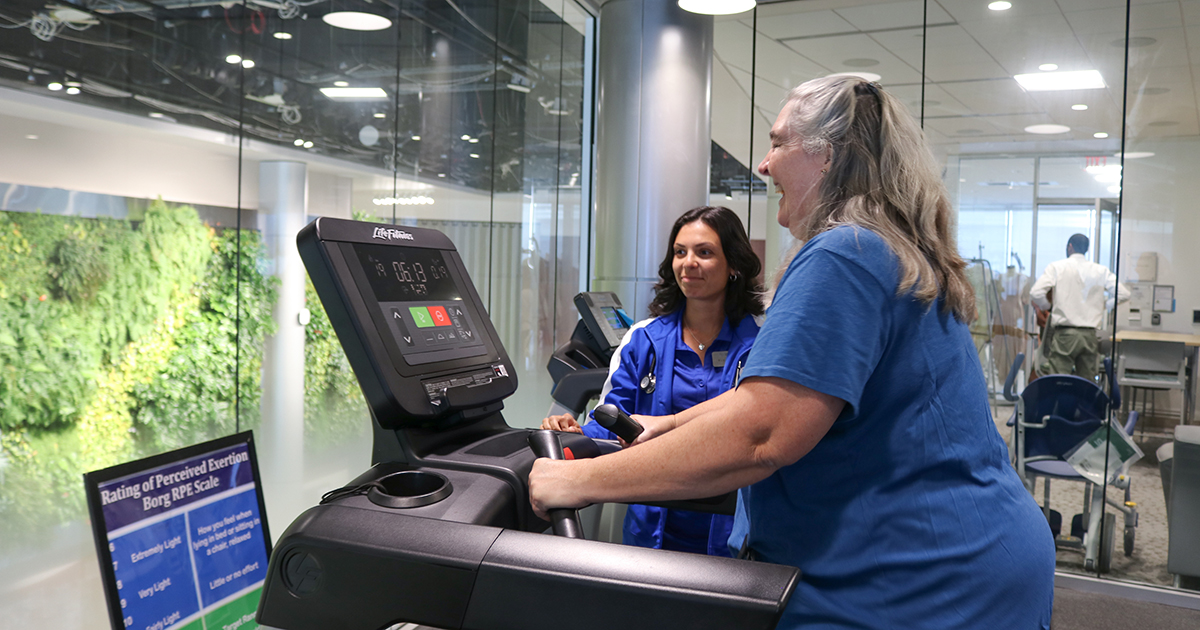 A client walks on a treadmill with a view of the Living Wall on STAR Campus while a master's student in clinical exercise physiology intermittently monitors her heart rate as part of exercise counseling. 
