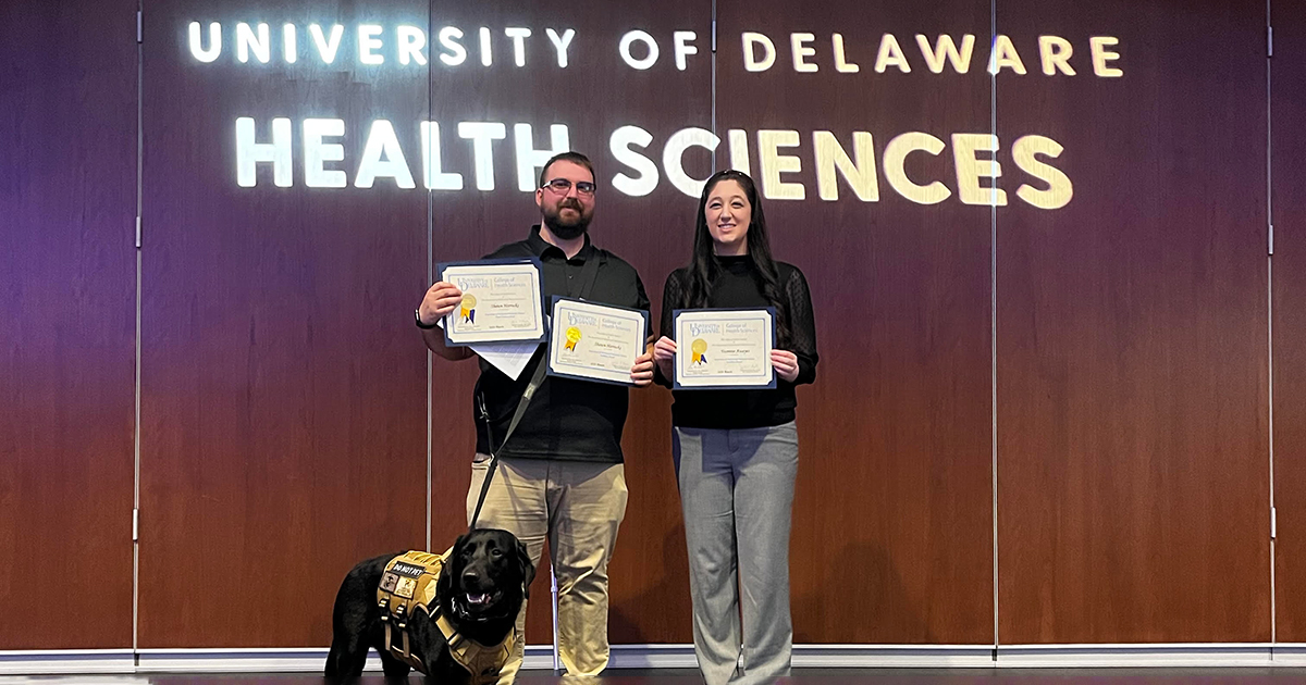 Medical diagostics senior Shawn Horrocks and his service dog, a black Labrador named Vinny, stand with fellow Medical and Molecular Sciences classmate Yasmine Awayes in the College of Health Sciences Audion showing holding MMSC Department awards bestowed upon them.