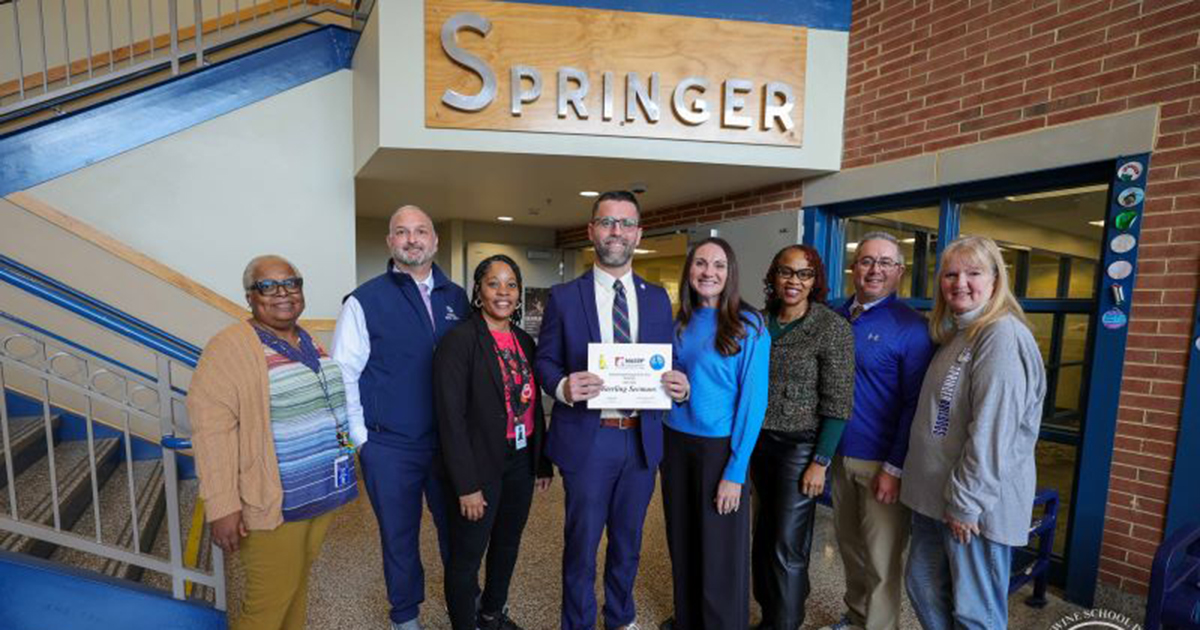 University of Delaware alumnus Sterling Seemans, principal of Springer Middle School in the Brandywine School District, received the 2026 Delaware Principal of the Year Award in January. Seeams, poses with others, while holding a certificate with the words Springer on the wall above his head, to represent Springer Middle School, where he is principal.