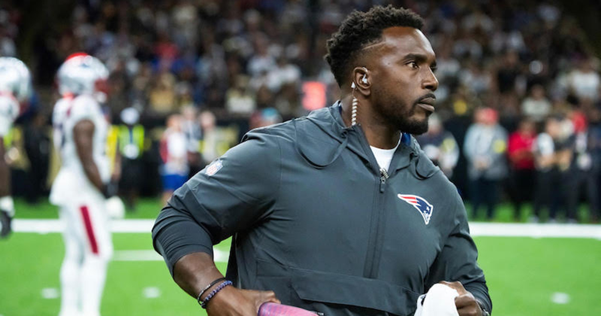UD physical therapy alumnus Michael Akinbola, director of rehabilitation for the New England Patriots, stands on the football field during a time out with a towel in his hand and holding water bottles on his hip.