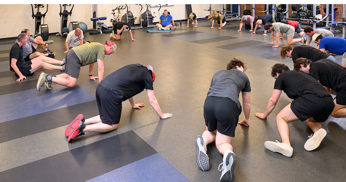 Veterans and member of UD's men's ice hockey team are on their knees with palms down on the floor, in a circle, participating in a high-intensity workout.