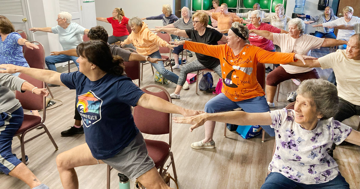 Community members participate in chair yoga with their arms outstretched while seated at the Weston Senior Center.
