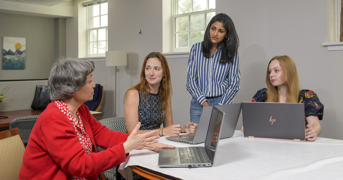 UD researchers and doctoral students gather around laptops at a table to discuss research on an AI chatbot that can be used to help people with disabilities. 