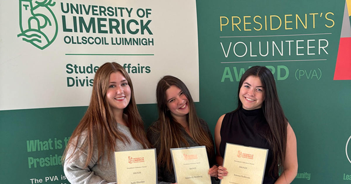 Honors nursing majors Aoife Riordan, Kim Steinberg and Emma Holleran received the President’s Volunteer Service Bronze Award from the University of Limerick for teaching English to Ukrainian refugees as part of their clinicals.  Here, they're standing with certificates with the University of Limerick President's Volunteer Award green and white backdrop. 