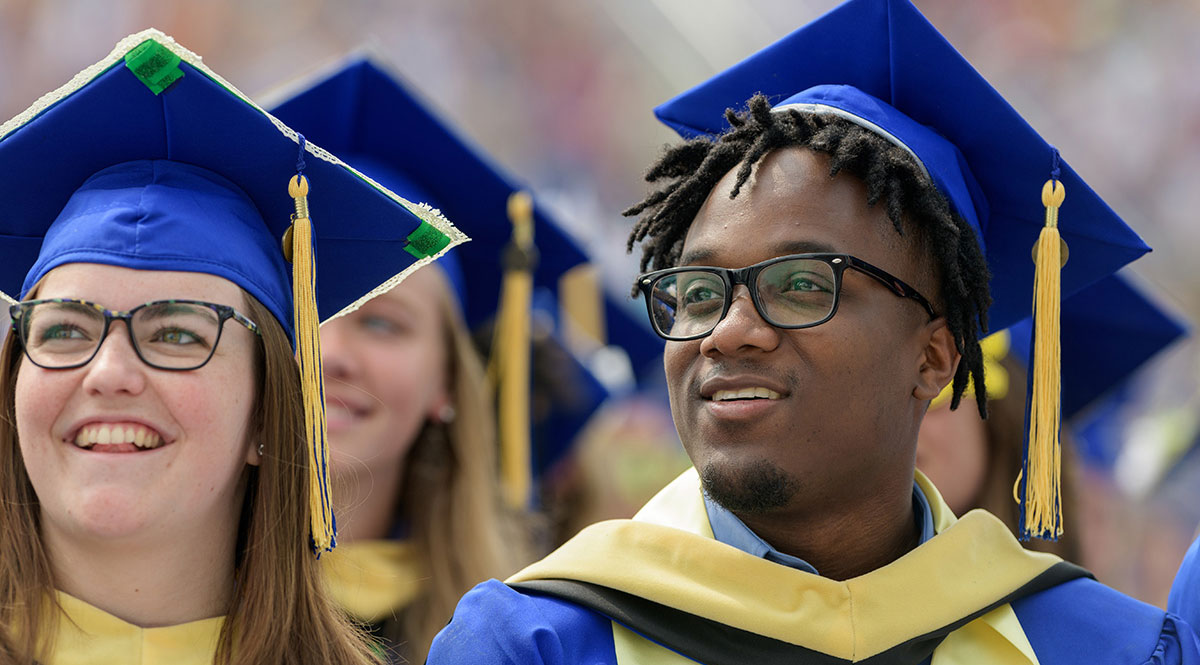 A male and female, dressed in blue robes, smile at their graduation from the University of Delaware. 