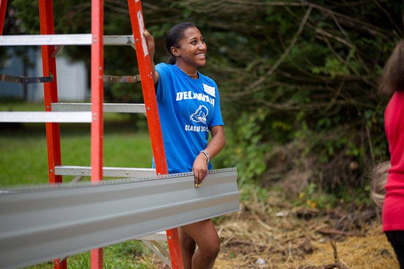 a community engagement scholar leans near a ladder on a construction site