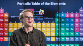 John Hill in front of a Periodic Table.