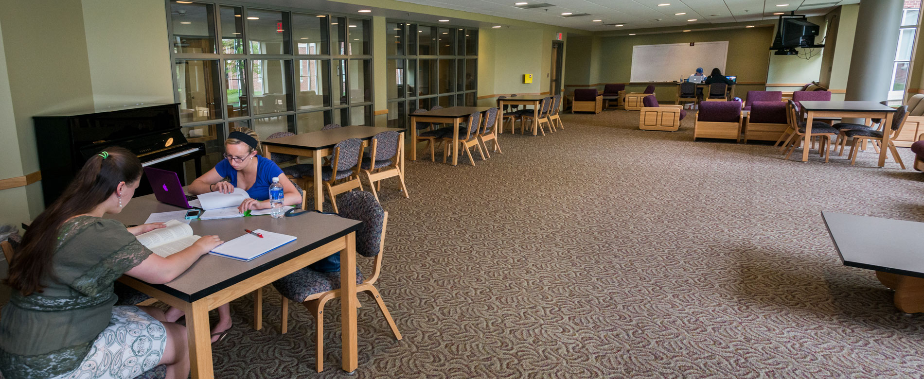 Students studying in a large lounge area with tables and comfortable chairs