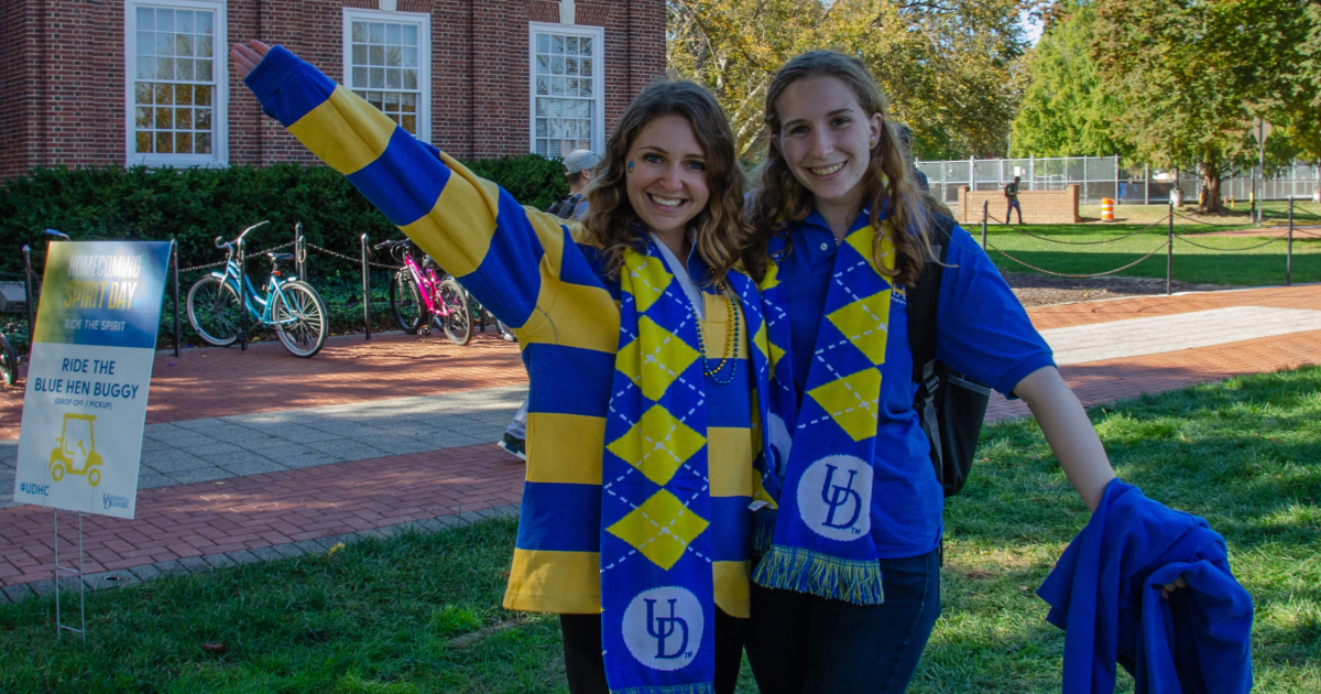 Two students in blue and gold UD clothing pose on The Green