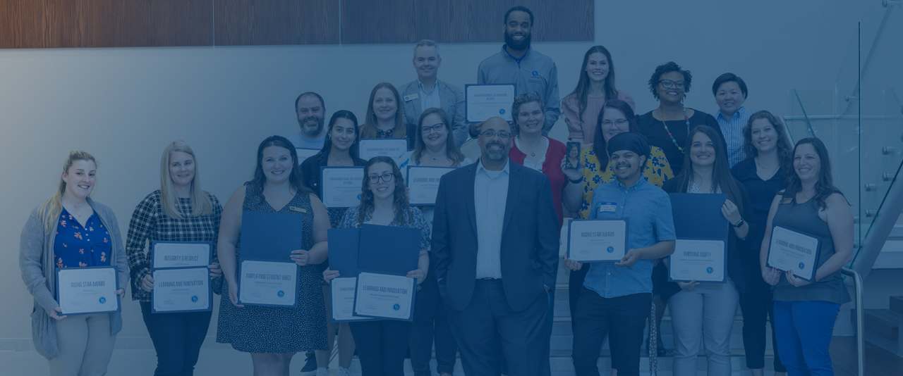 recipients of 2023 Student Life End-of-Year awards pose with VP José Riera in front of a glass-enclosed staircase