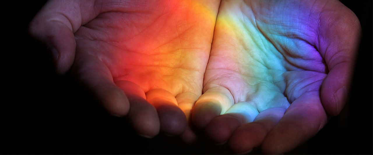 Open hands with a rainbow reflected on the palms