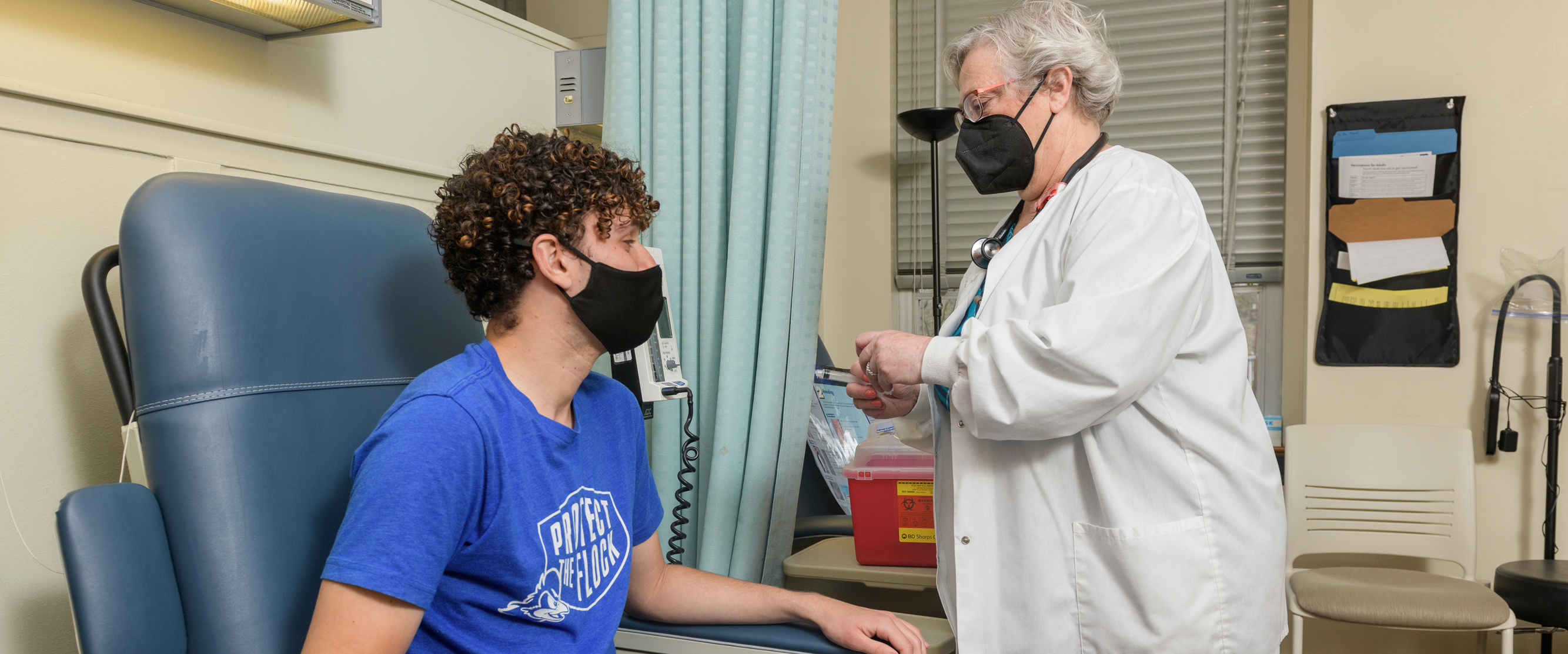 a masked SHS employee gives a vaccine to a masked student