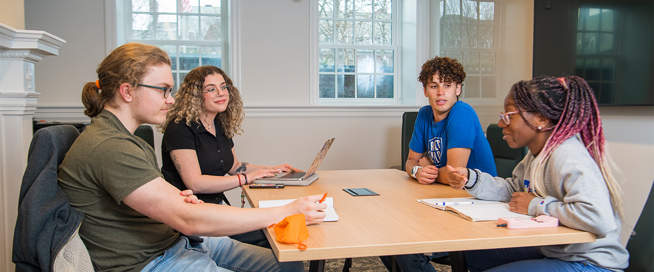 Four students collaborating in a small meeting room