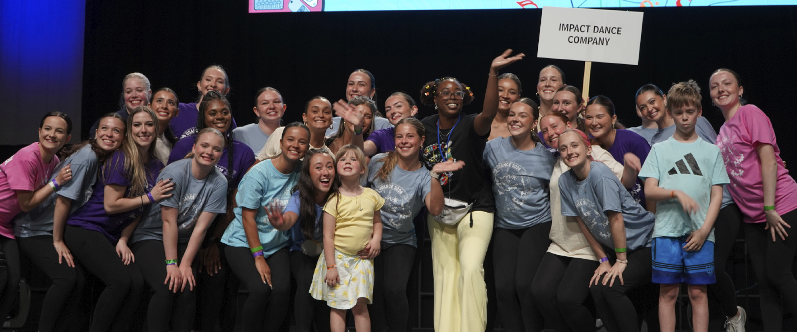 students stand together on stage under a screen that says "$20,000 raised".