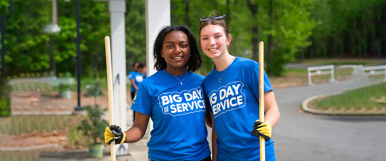 Two students with gardening gloves and rakes