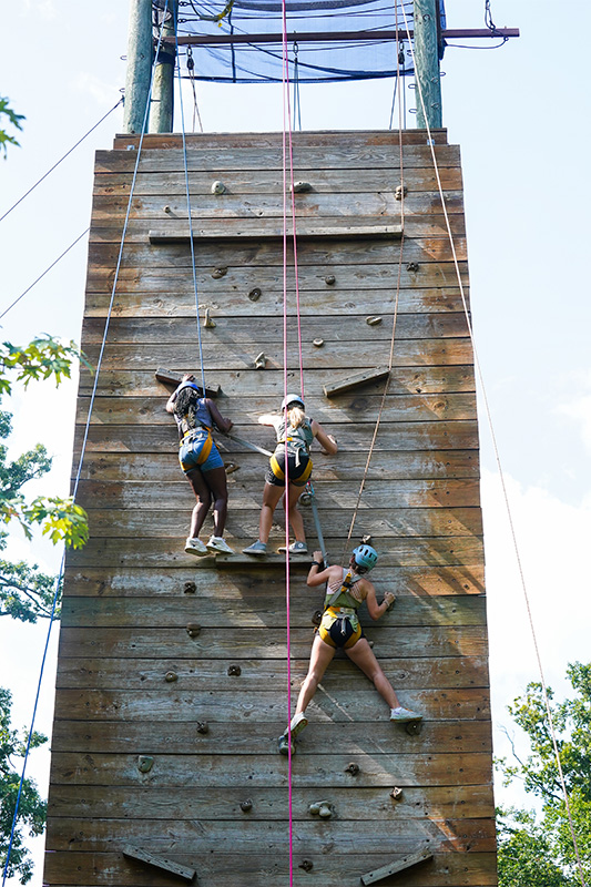 Three students climb an outdoor rock wall