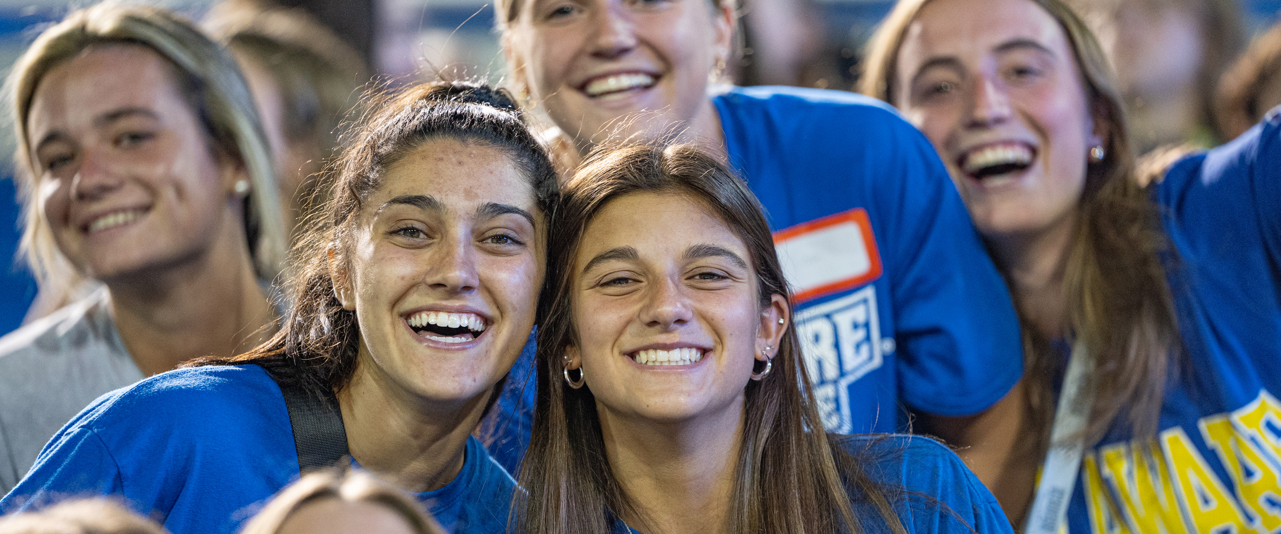 students wearing Blue Hens t-shirts smile at a UD football game at night