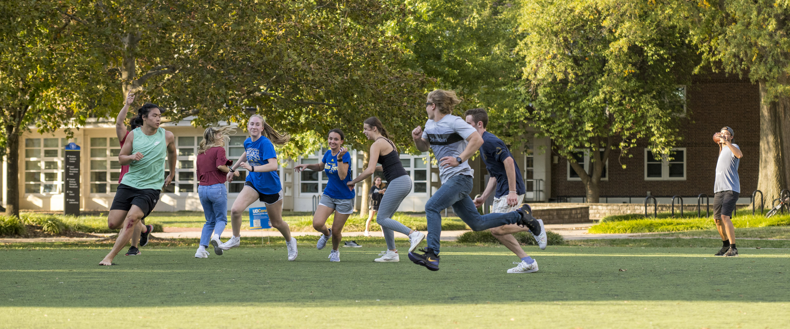 a group of students play football on the green space outside a University of Delaware residence hall.