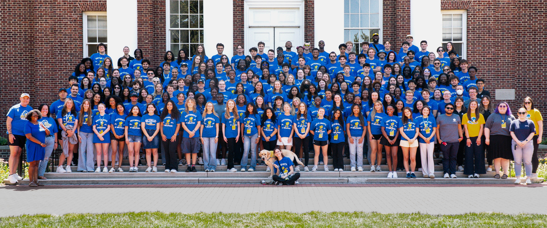 RLH staff and student leaders wear blue shirts and pose on the steps of UD's Memorial Hall.