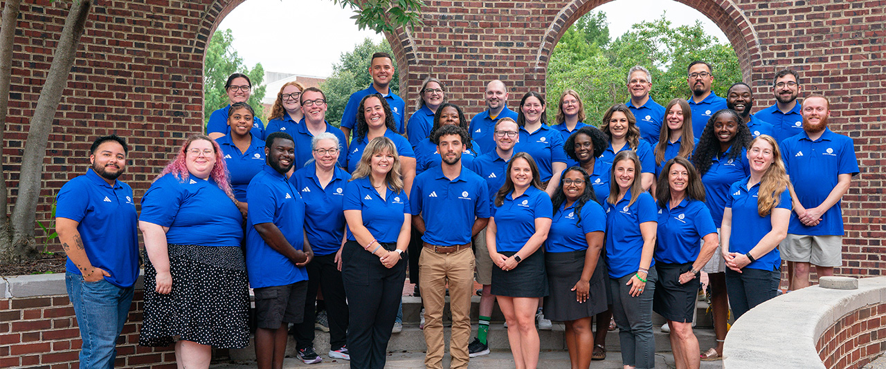 University of Delaware Residence Life & Housing staff members pose in blue shirts on the steps of Caesar Rodney residence Hall.