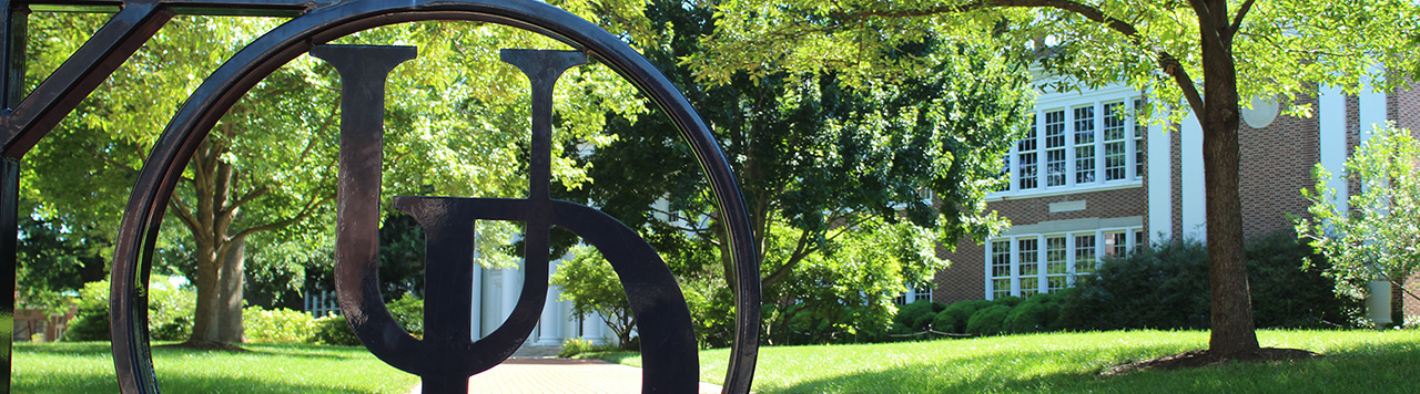 UD gate in front of on-campus building and green trees.
