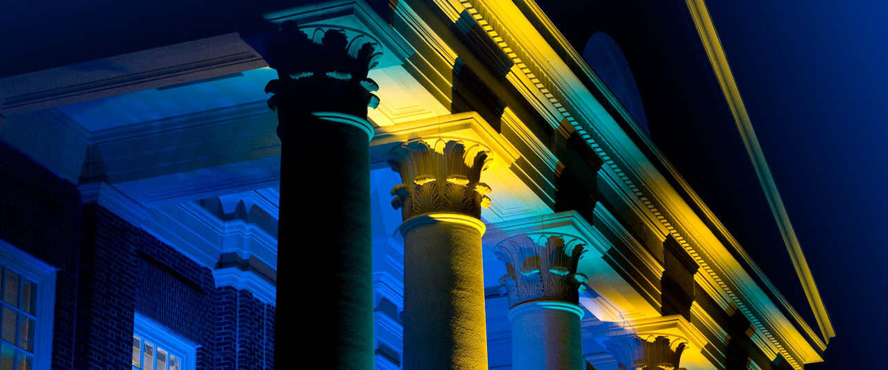 Columns of a UD Building on campus being illuminated by Blue and Gold lighting.