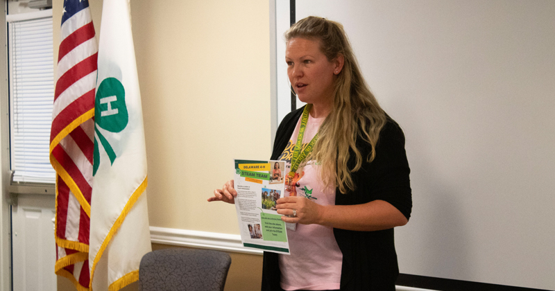 Twila Parish-Short holds the STEAM Team information flier and explains what the STEAM Team entails to a group of youth and adults sitting around her. 
