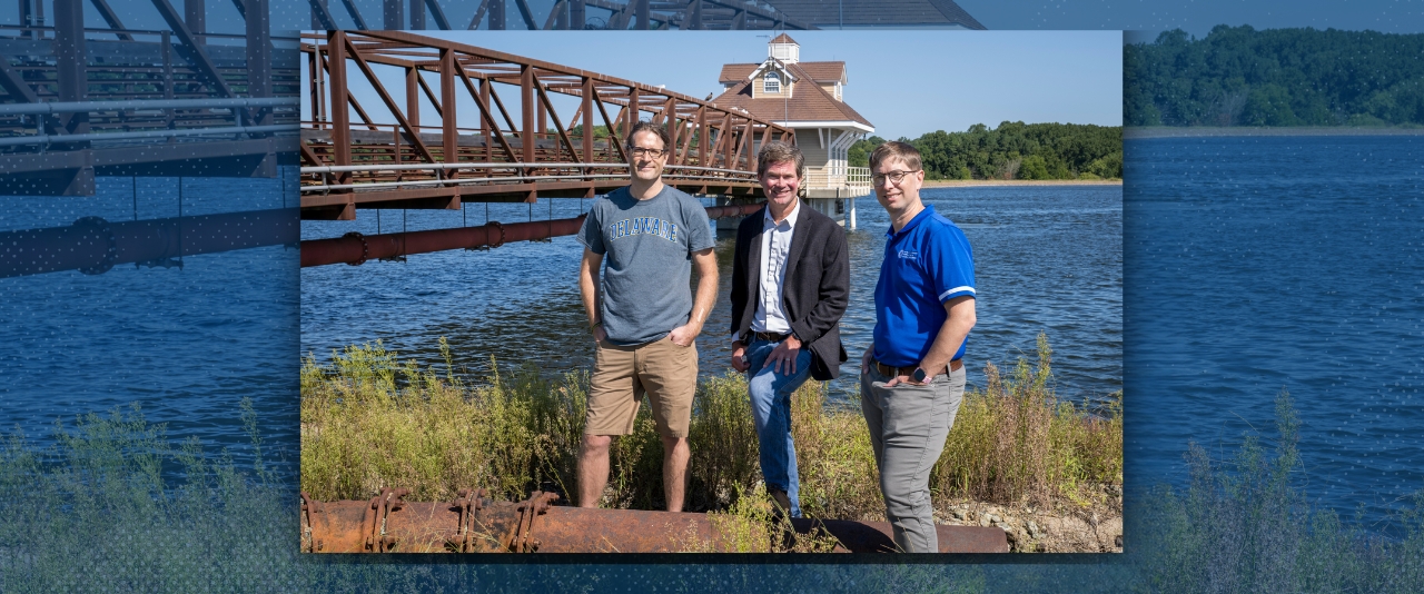 Three faculty members stand next to the Newark Reservoir