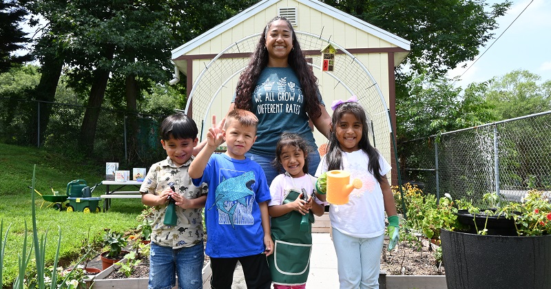 Diana Mercado, early childhood administrator at Pirulo’s Child Care and Learning Center, smiles with children in front of the garden she grew with the support of UD’s Let’s Grow Outside! initiative. 