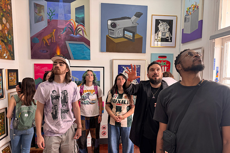 A group of visitors stands in a gallery, looking up at colorful contemporary artworks displayed on the walls.