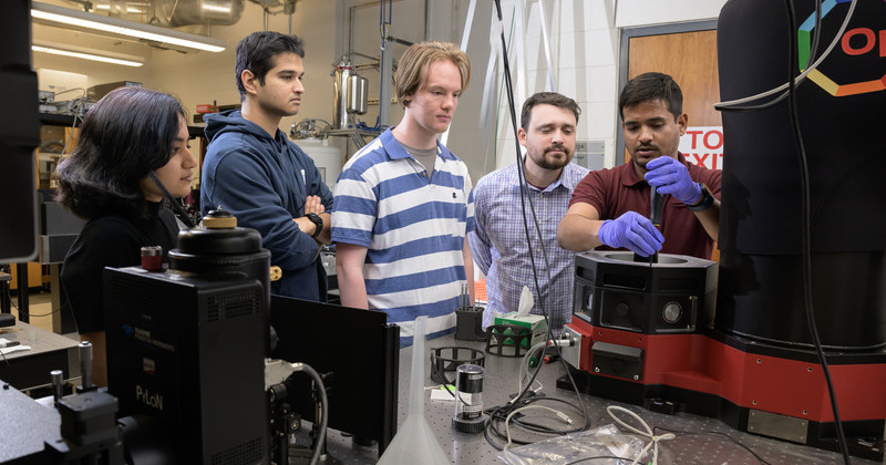 Chitraleema Chakraborty, Aqiq Ishraq, Alexander Hutchinson, Collin Maurtua and Muhammad Hassan Shaikh gather around a cryostat system used for low-temperature optical and electrical measurements in next-generation magnetic sensing research.