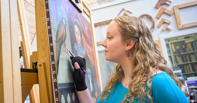 Elizabeth Glander, a Winterthur/University of Delaware Program in Art Conservation Fellow, inpainting on a Dutch style oil on canvas painting “Portrait of a Dutch Girl with a Parrot and Basket of Fruit,” 1646, by an unknown artist.