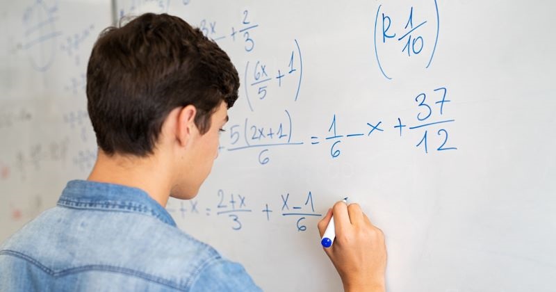 A student completes an algebra problem at the whiteboard.