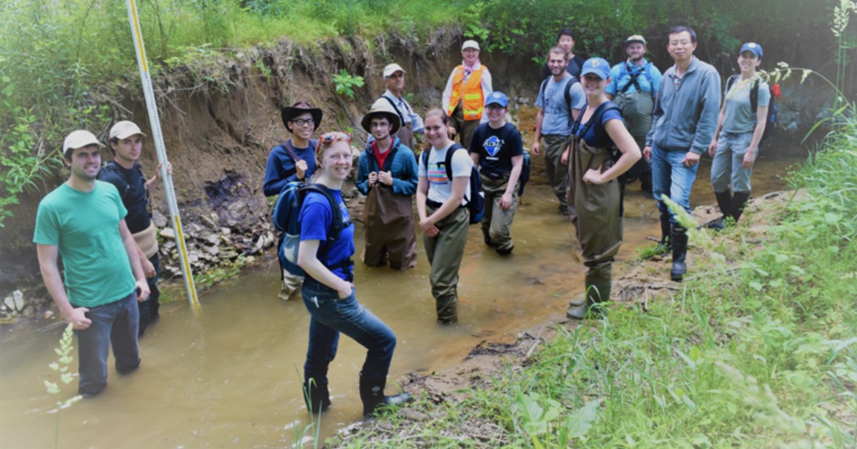 Grant Jiang and Nate Sienkiewicz (center) in cowboy hats along with other researchers and students along a legacy sediment streambank. Grant Jiang and Nate Sienkiewicz (center) in cowboy hats along with other researchers and students along a legacy sediment streambank.