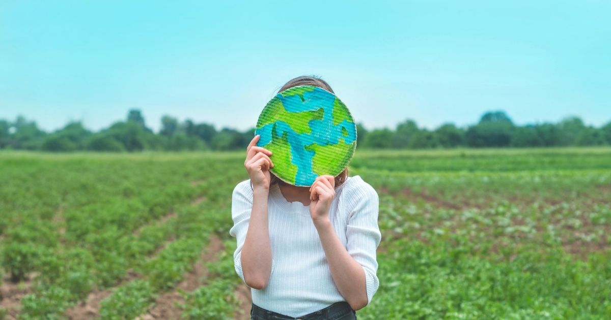 A child holding up a cutout of Earth, standing in a field.
