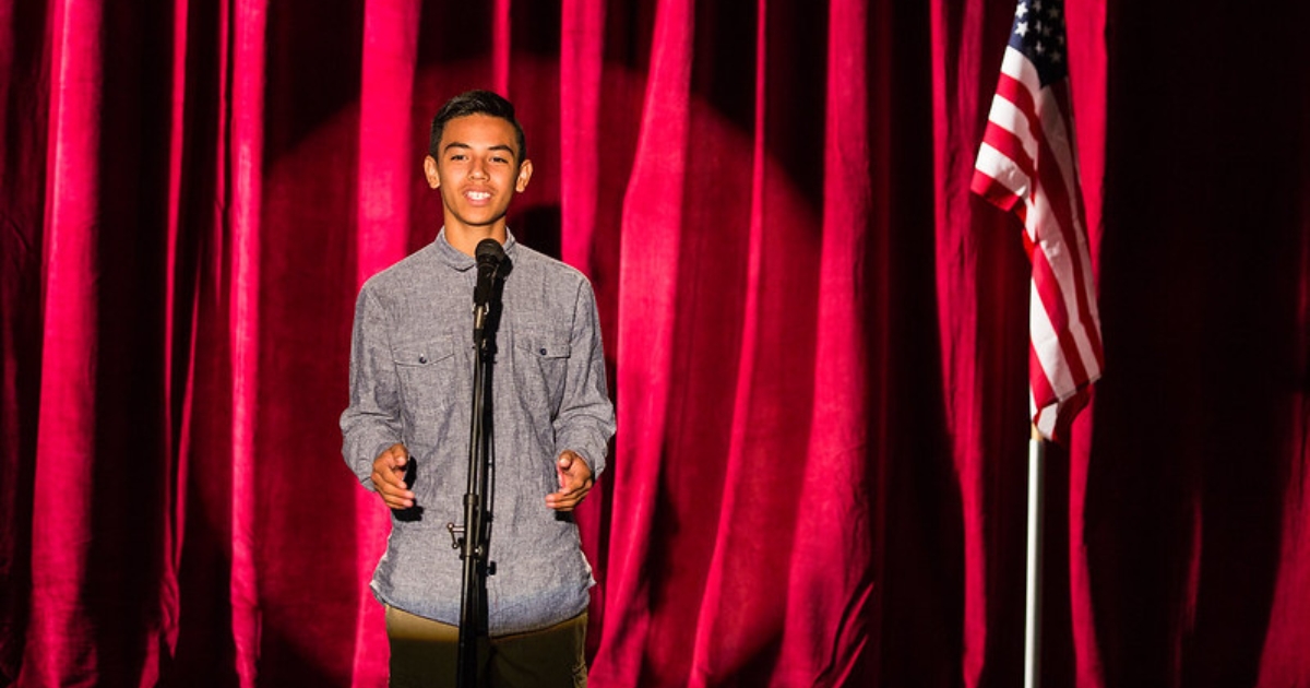 A young man speaking in front of an audience at a talent show.