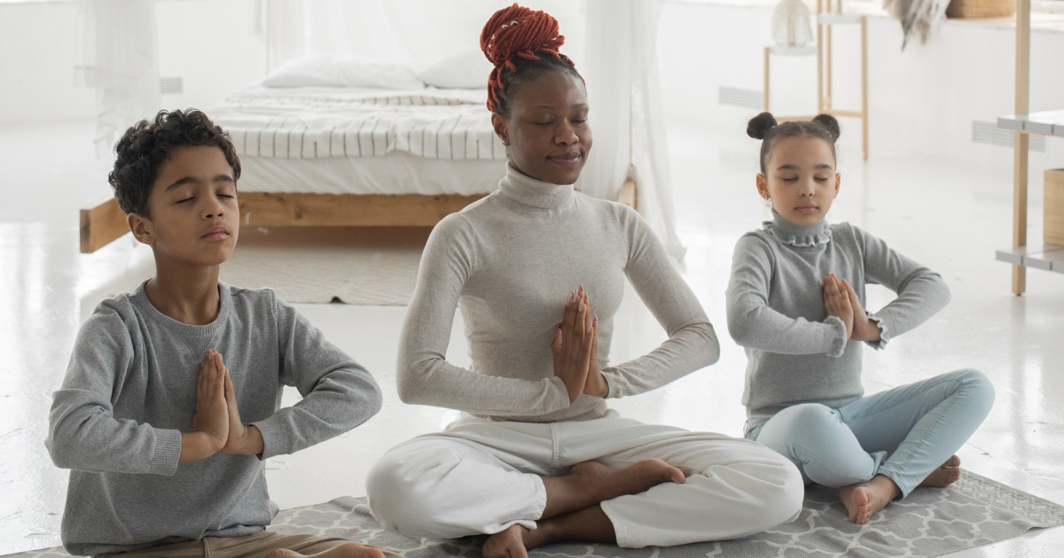 A mother and two children sitting on the floor and meditating to reduce stress.