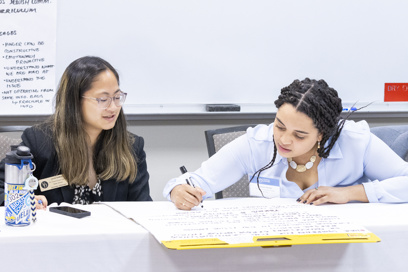 Two people sitting at a table together writing notes on a pad of paper