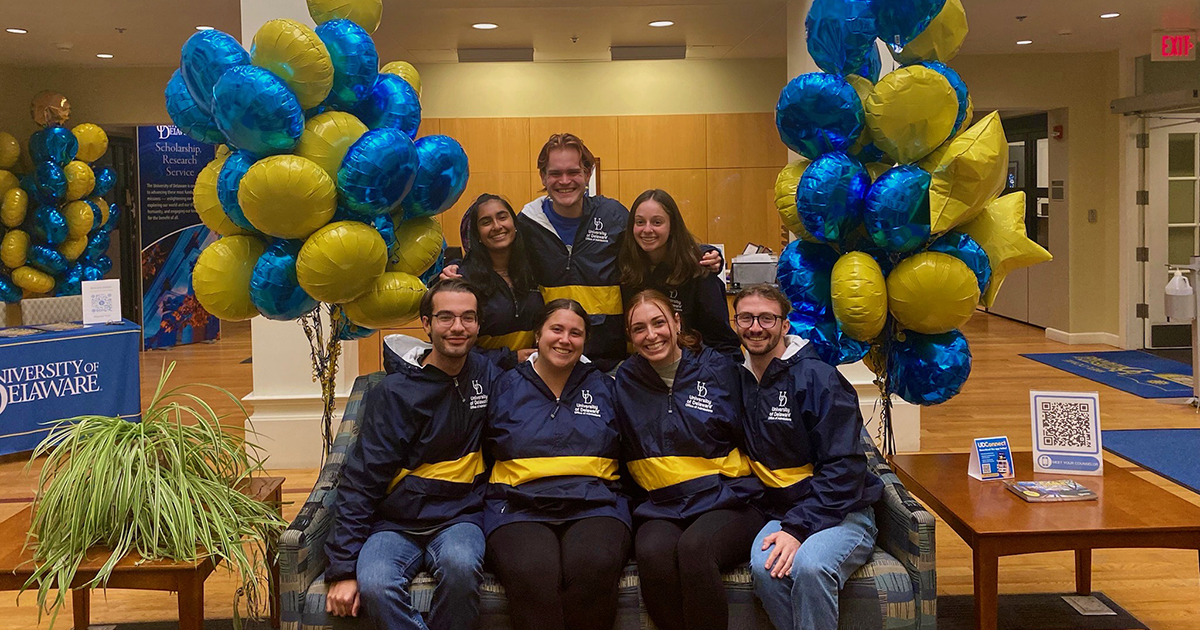 Blue Hen Ambassadors pose on couch surrounded by blue and gold balloons