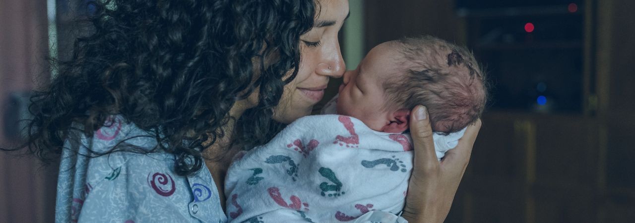 Smiling woman holding newborn baby close to her face