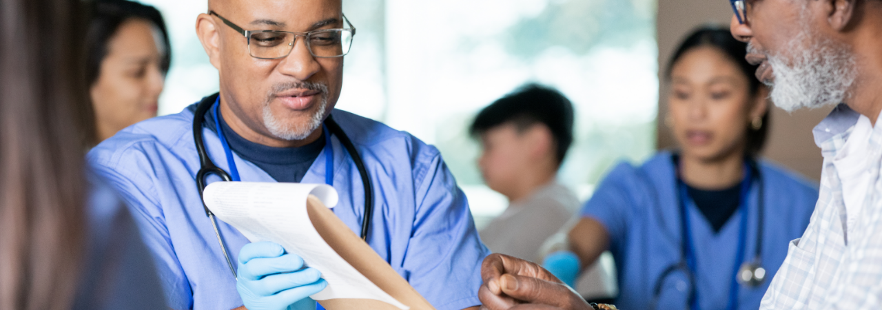 A clinician wearing a stehoscope holds a clipboard in front of a patient