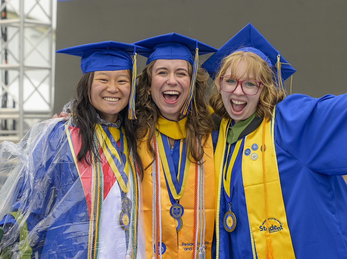Three female students in caps and gowns pose for an image at commencement