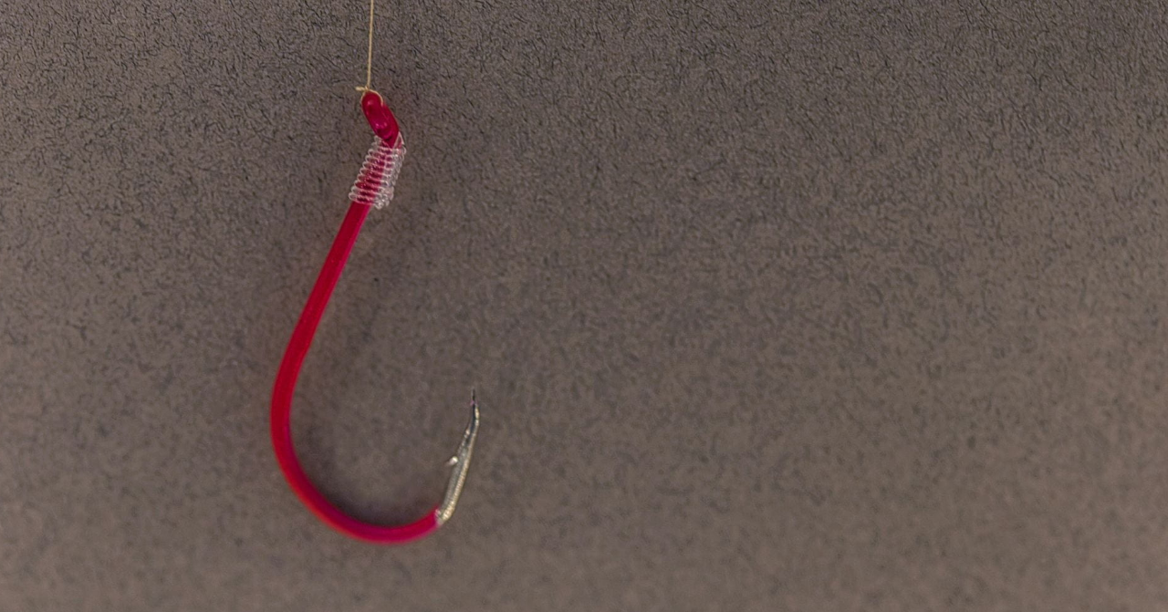 A red fishing hook hangs from a string in front of a tan background