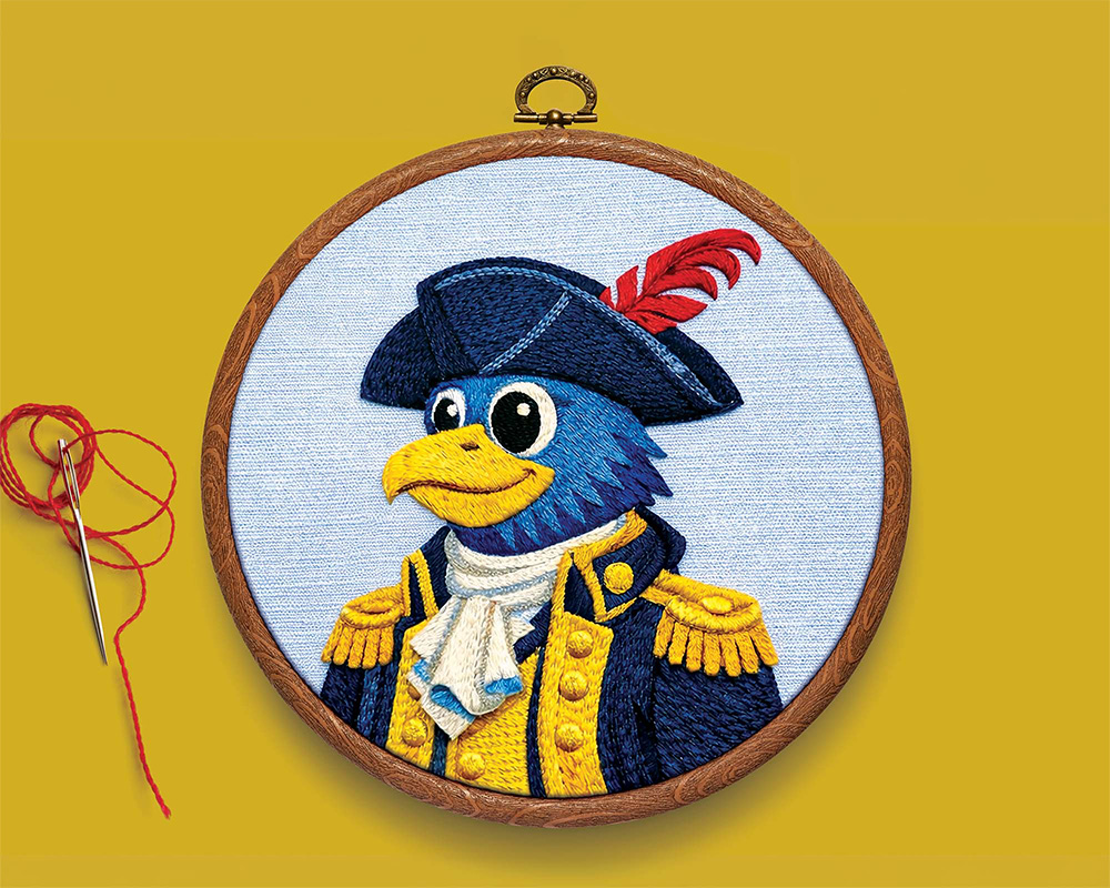 Embroidered illustration of the University of Delaware's Blue Hen mascot dressed in a Revolutionary War uniform inside a wooden embroidery hoop.