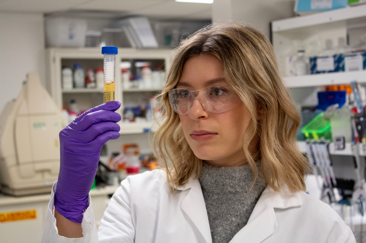 Graduate Student, Mackenzie Sharp, holds up a test tube in the lab.