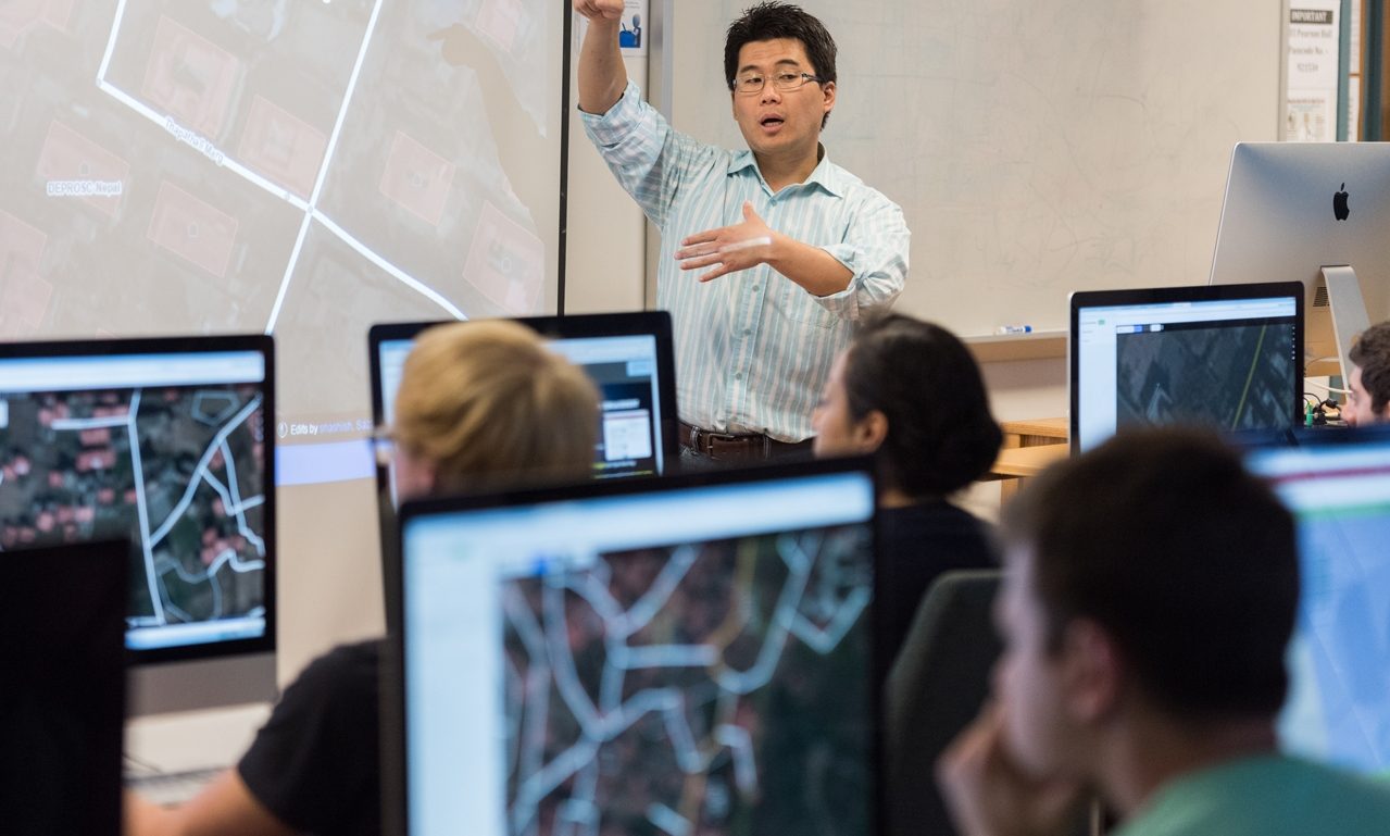 instructor at front of classroom with students looking at computers with GIS software displayed