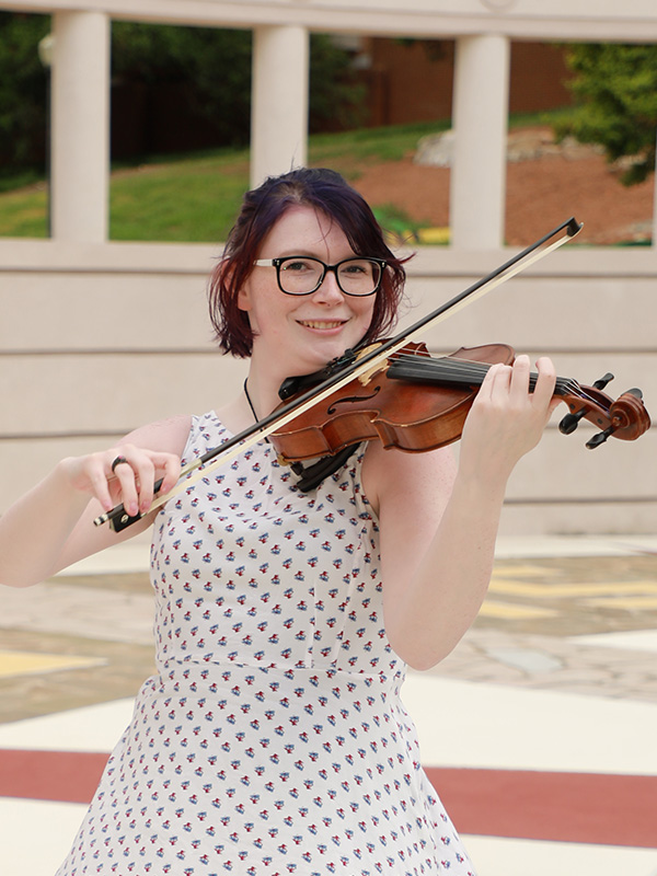 Young woman playing a violin in an outdoor courtyard.