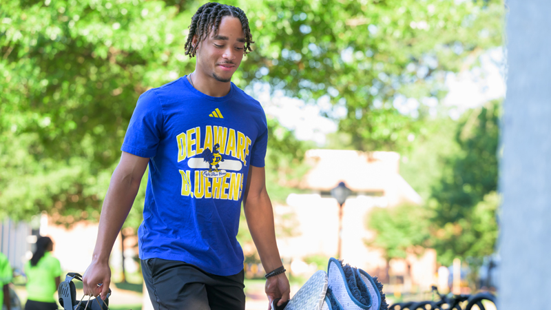 a student wearing a UD shirt carries belongings into a residence hall on move-in day