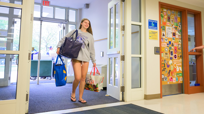 a student walks through the doors of a residence hall carrying belongings